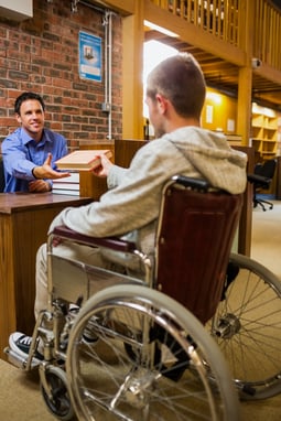 Male student in wheelchair at the counter in college library
